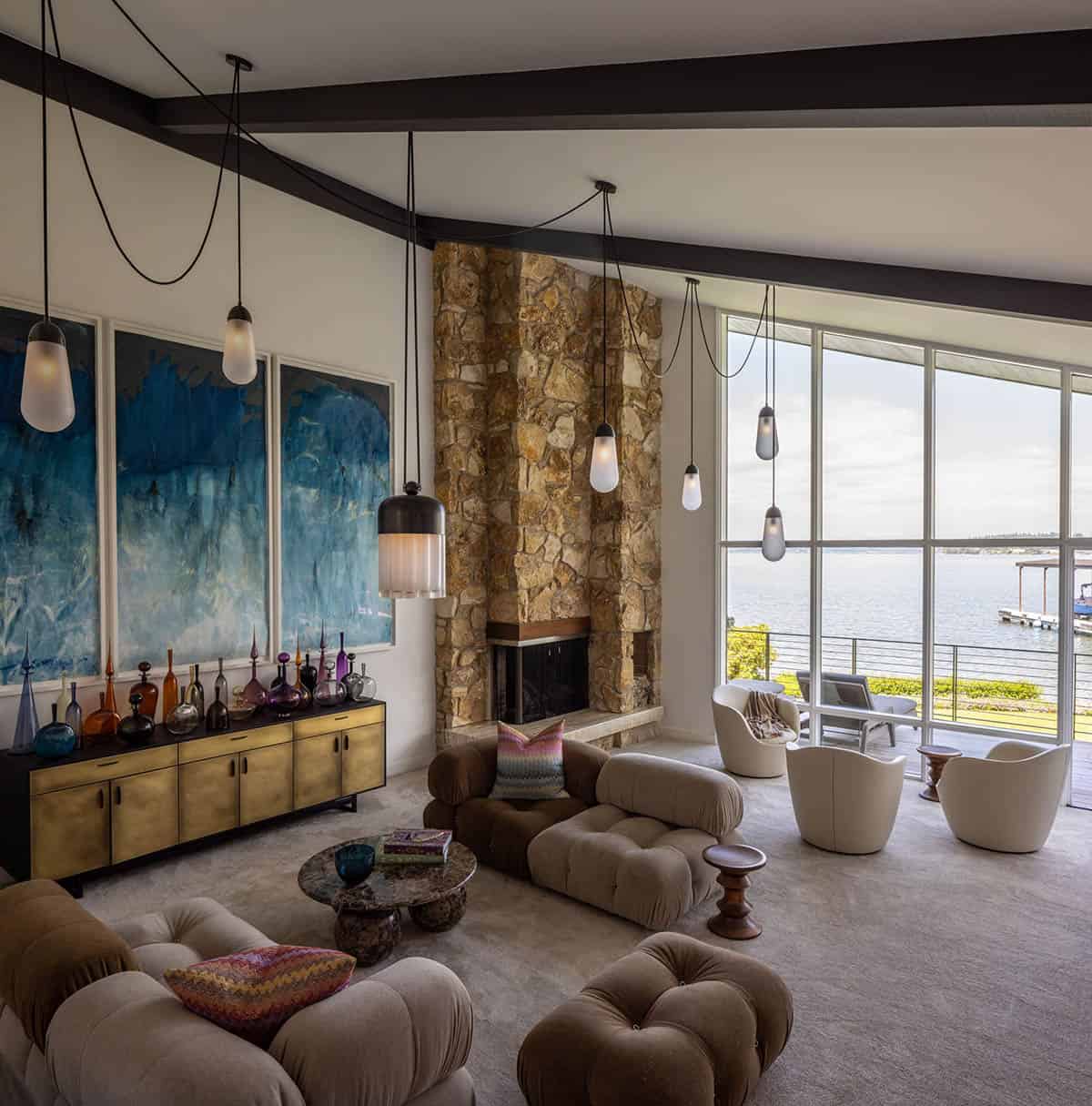 Living room with stone fireplace, modular sofa, brass credenza, glass bottle collection, and lake views