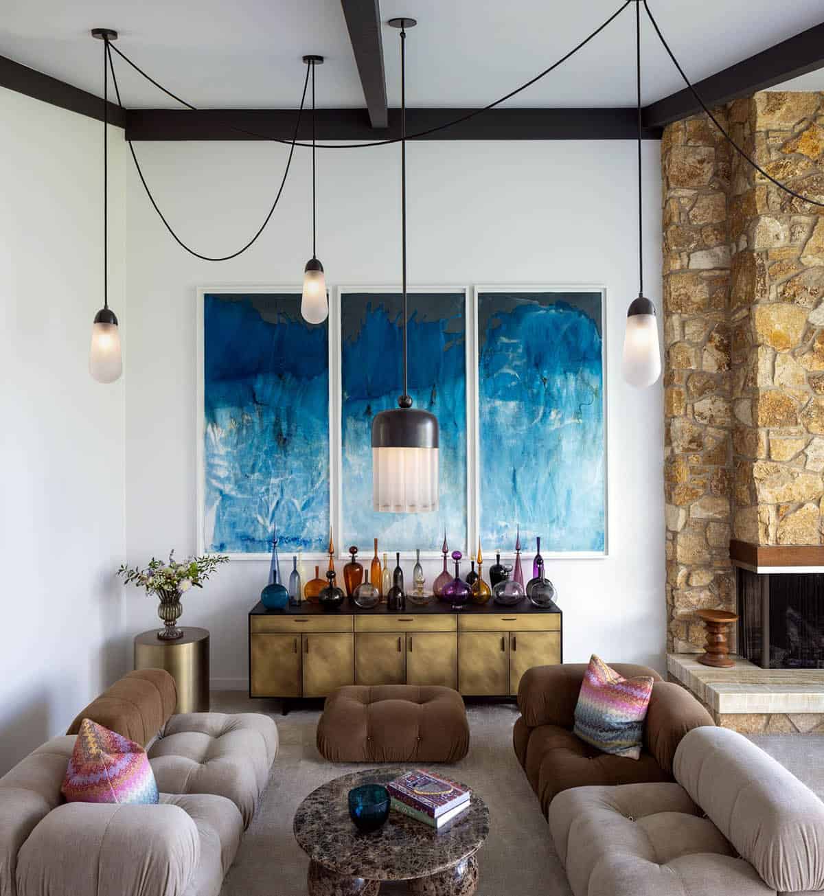 Living room detail with blue abstract triptych, brass credenza, glass bottle collection, and pendant lights