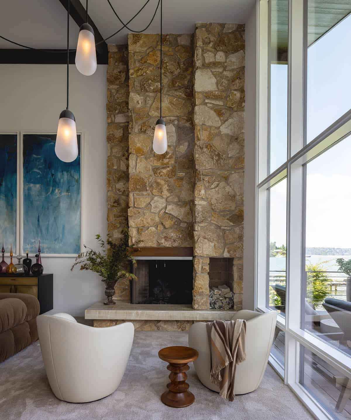 Stone fireplace with floor-to-ceiling surround, white lounge chairs, and lake views through tall windows