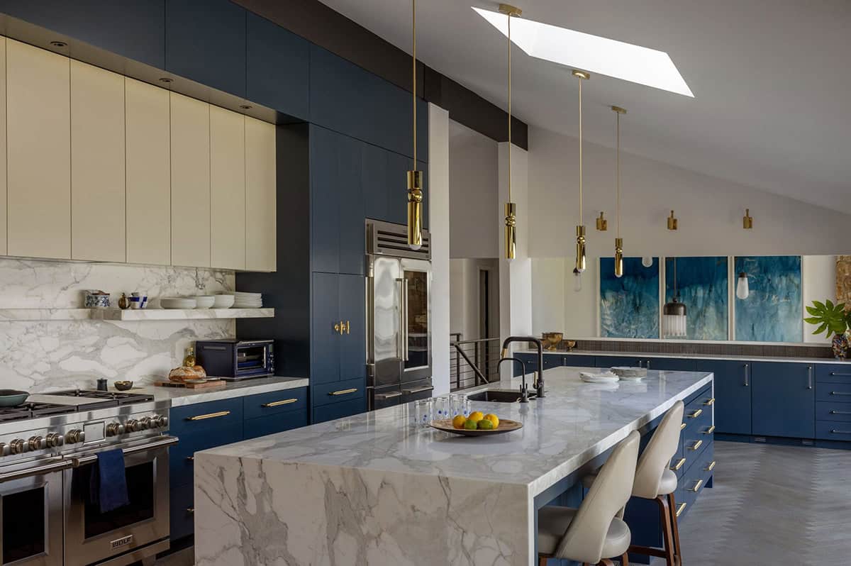 Mid-century modern kitchen with navy blue and cream cabinets, marble island, brass pendants, and skylight