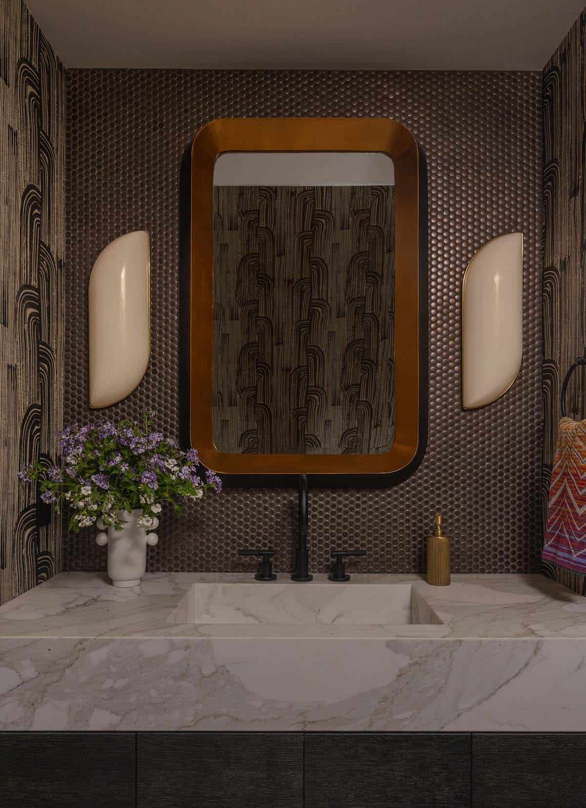 Powder room with penny tile walls, geometric wallpaper, copper-framed mirror, and marble sink