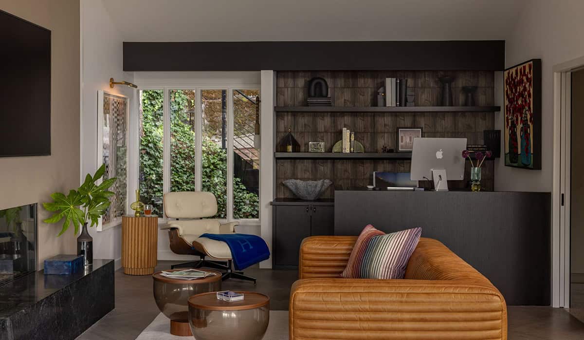 Home office and lounge with Eames chair, leather sofa, dark built-in shelving, and ivy-covered garden window