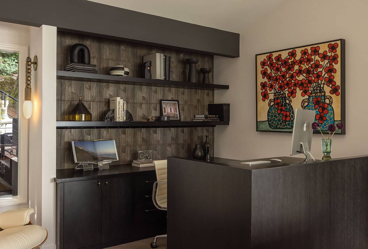 Home office with dark built-in desk, open shelving, textured wallpaper, and bold floral painting