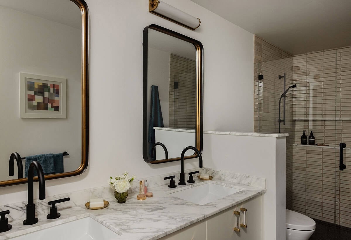 Guest bathroom with dual marble vanity, black matte faucets, gold-framed mirrors, and stacked tile shower