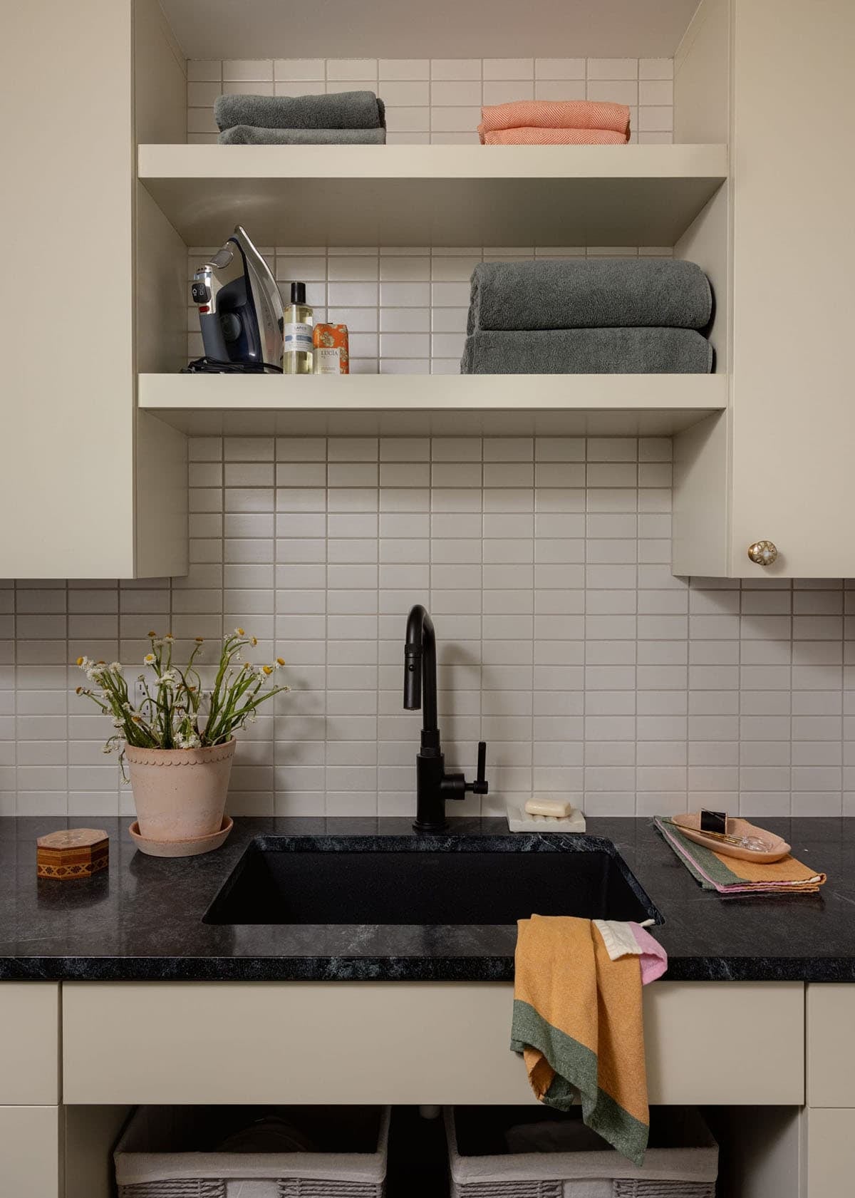 Laundry room with black undermount sink, matte black faucet, white subway tile backsplash, and open shelving with folded towels