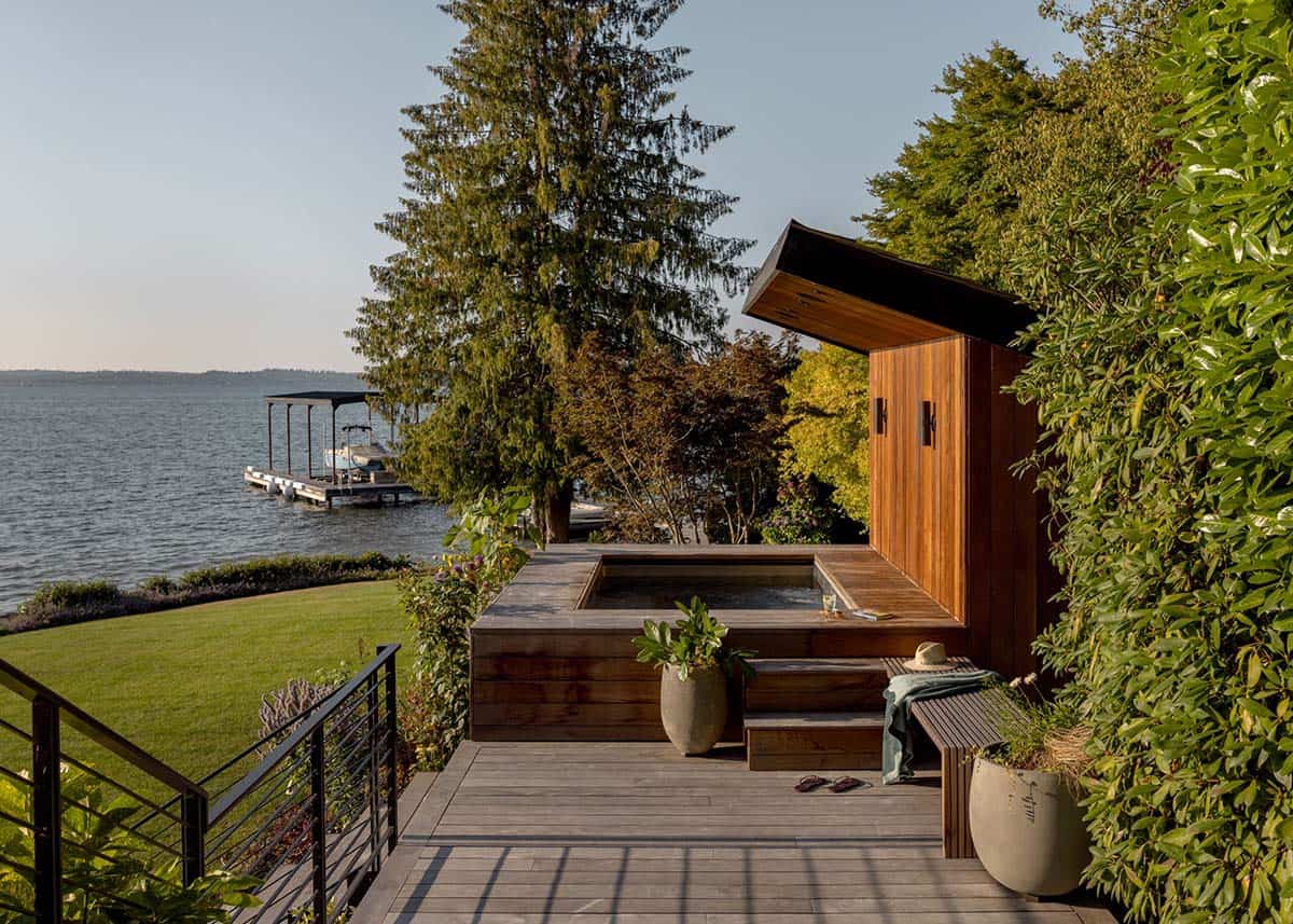 Cedar sauna and hot tub deck overlooking lake with dock, lush landscaping, and cable railing on Mercer Island
