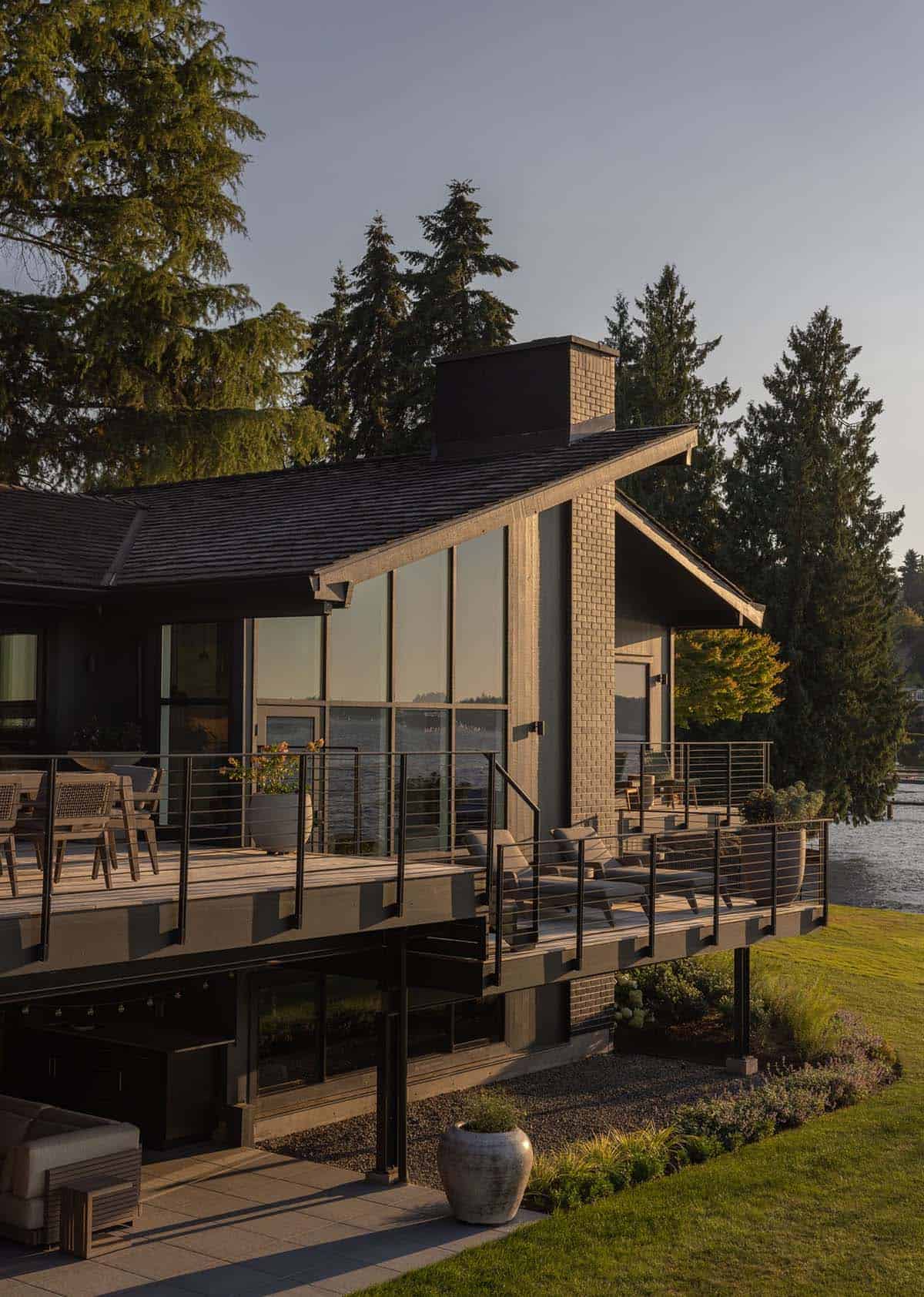 Mid-century modern waterfront home exterior at golden hour with wraparound deck, cable railing, and floor-to-ceiling windows