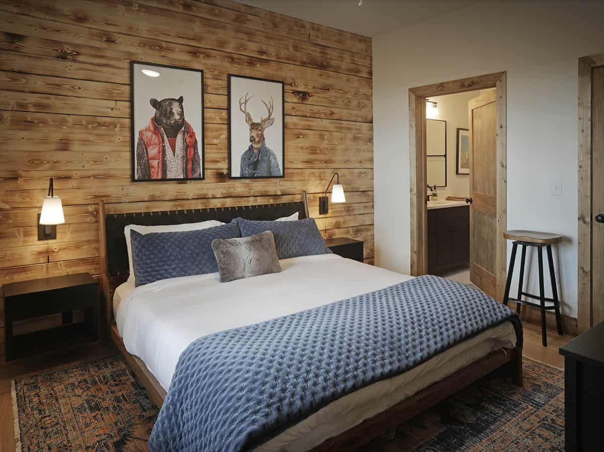Bedroom with knotty pine accent wall, blue velvet bedding, and whimsical animal portraits