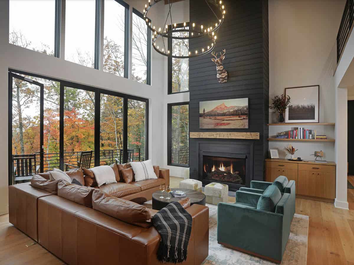 Double-height living room with leather sectional, black shiplap fireplace, and floor-to-ceiling windows