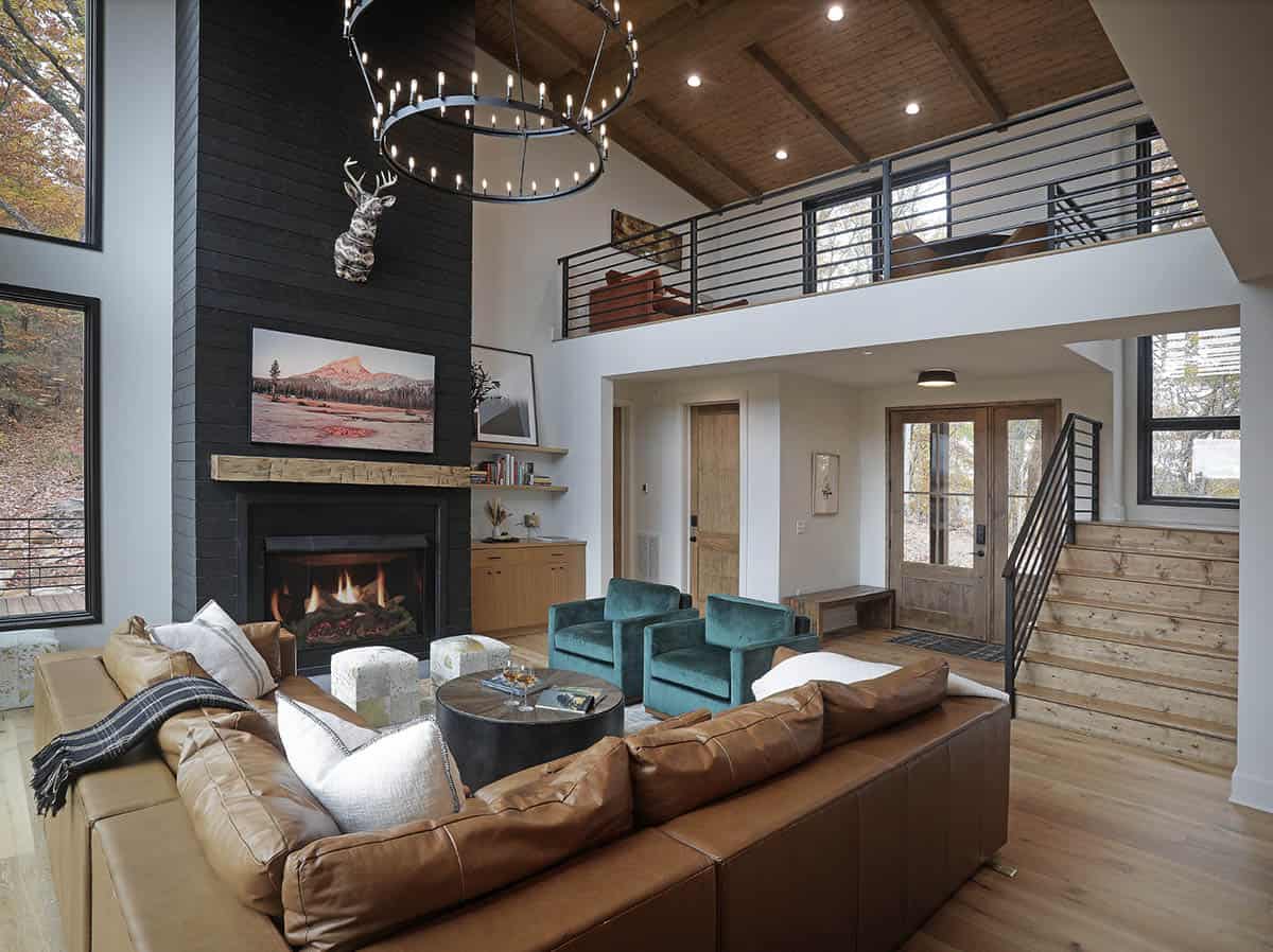 Living room with black shiplap fireplace, leather sectional, teal armchairs, and loft above