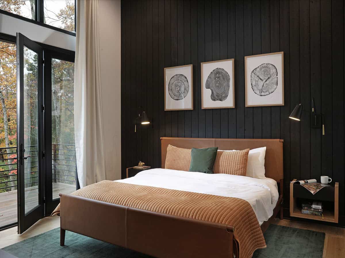 Dark shiplap primary bedroom with leather bed, tree-ring artwork, and forest balcony door