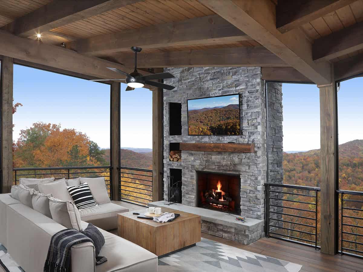 Screened porch with stone fireplace, outdoor sofa, and panoramic autumn mountain views