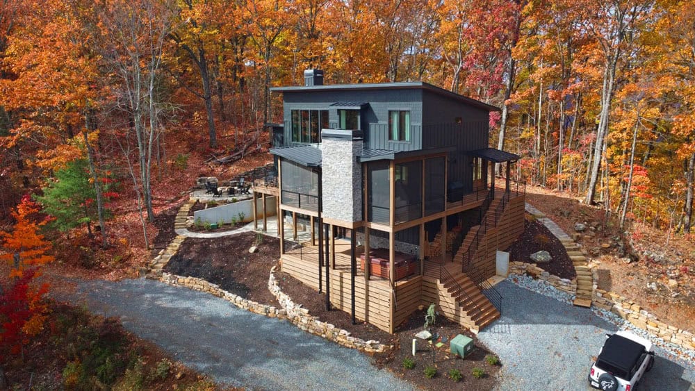 Aerial view of dark modern mountain home surrounded by fall foliage
