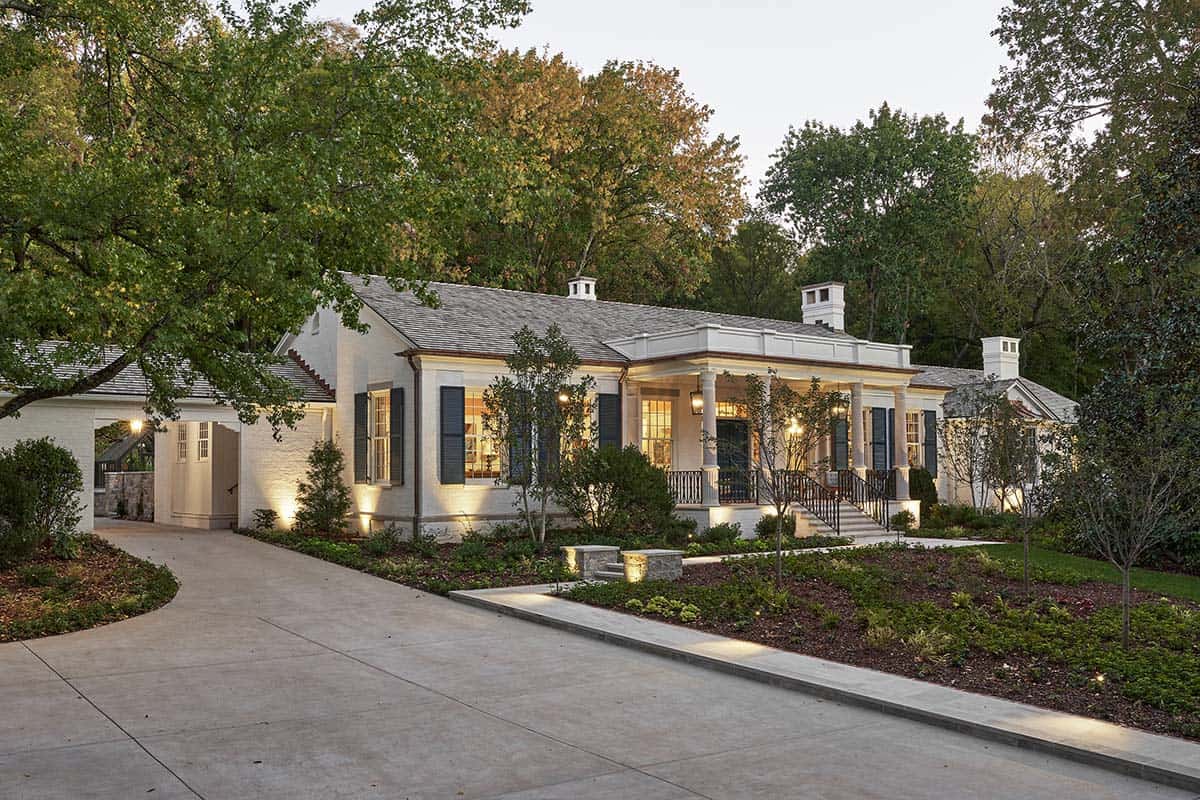 White painted brick colonial house at dusk with covered front porch, black shutters, and landscaped driveway