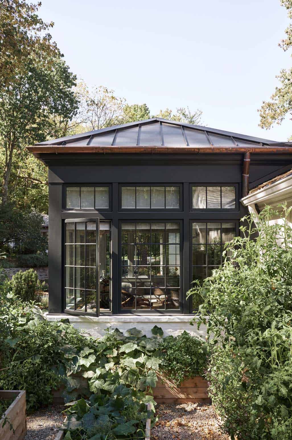 Dark steel-framed glass conservatory addition surrounded by vegetable garden beds