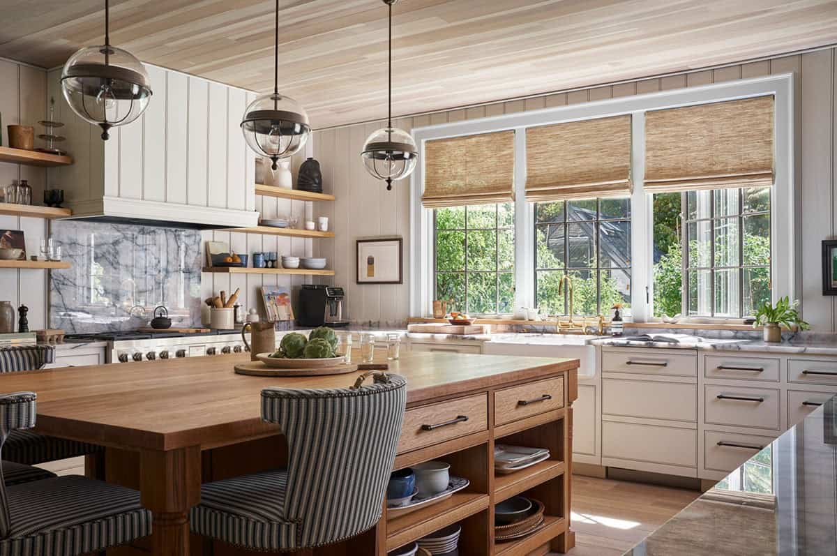 Warm kitchen with wood island, globe pendant lights, beadboard walls, and woven roman shades