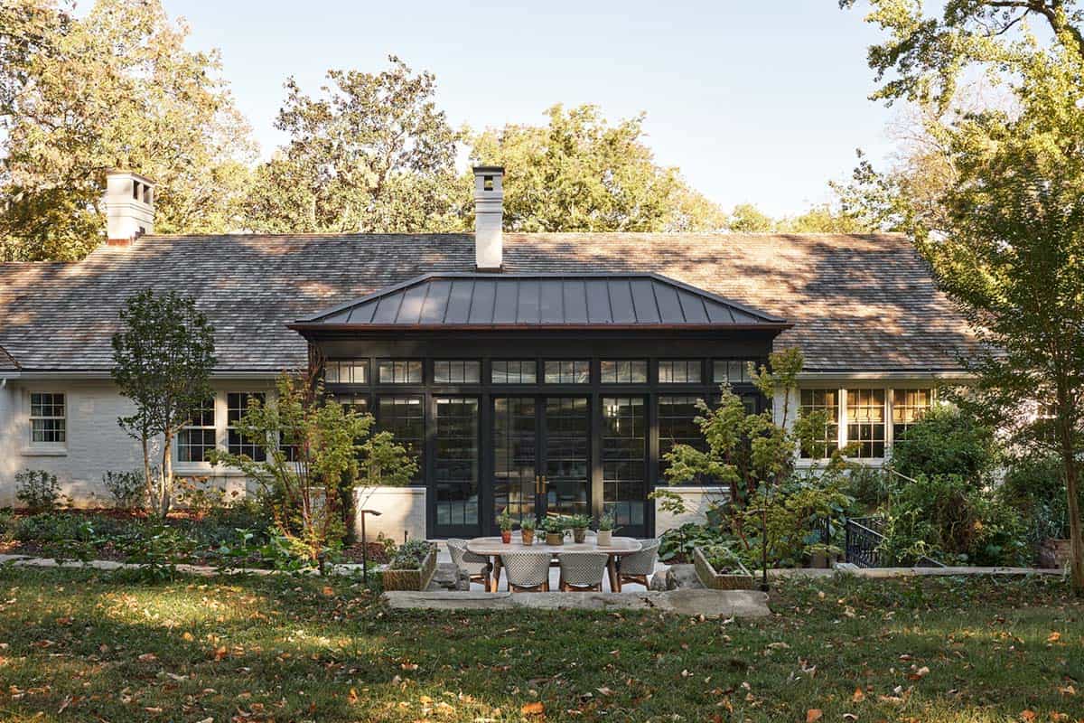 Rear exterior of white brick house with black steel conservatory addition and outdoor dining patio