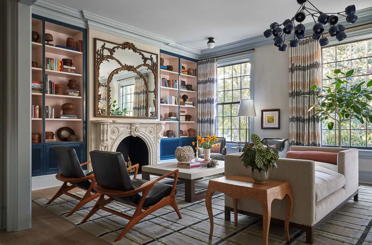 Living room with pink bookshelves, navy cabinets, ornate fireplace, and mid-century lounge chairs