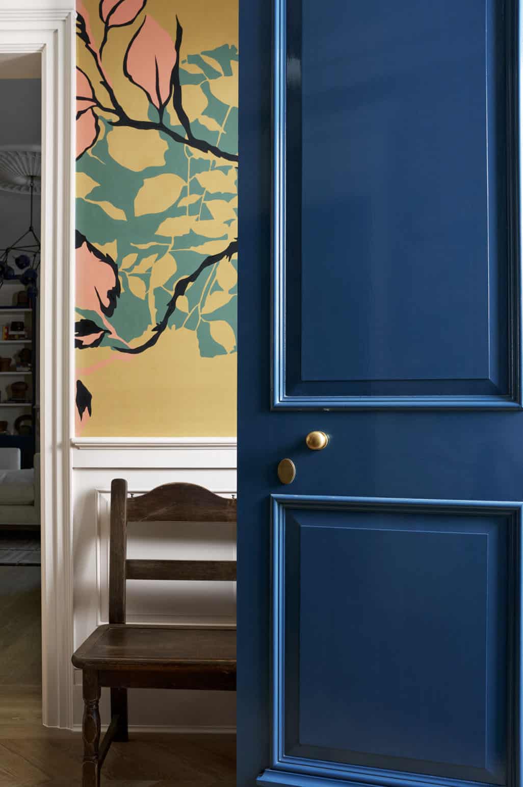 Glossy navy blue paneled door with brass knob opening to foyer with bold botanical wallpaper mural