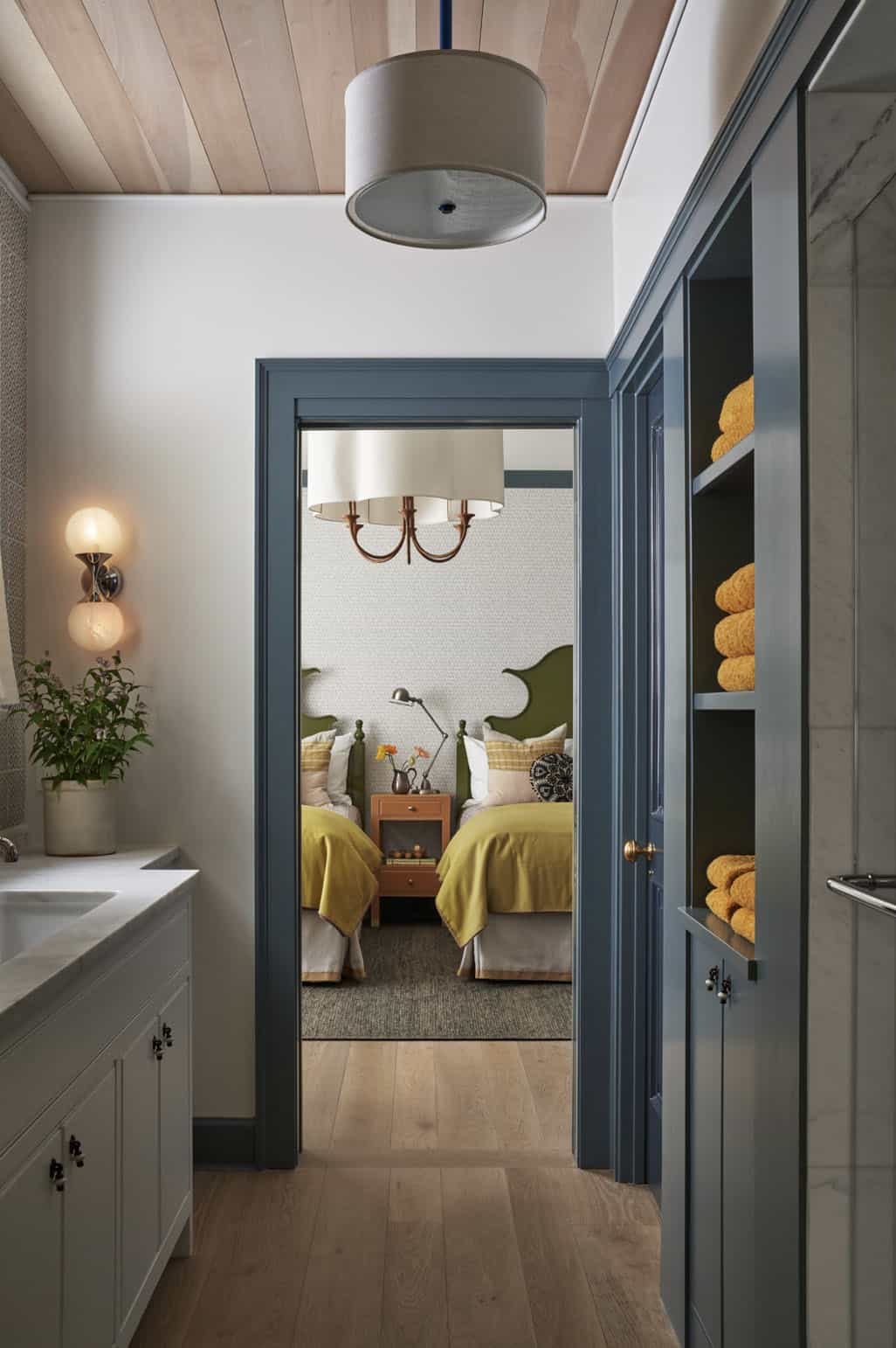 Bathroom hallway in slate blue with view into twin bedroom featuring olive headboards and yellow bedding