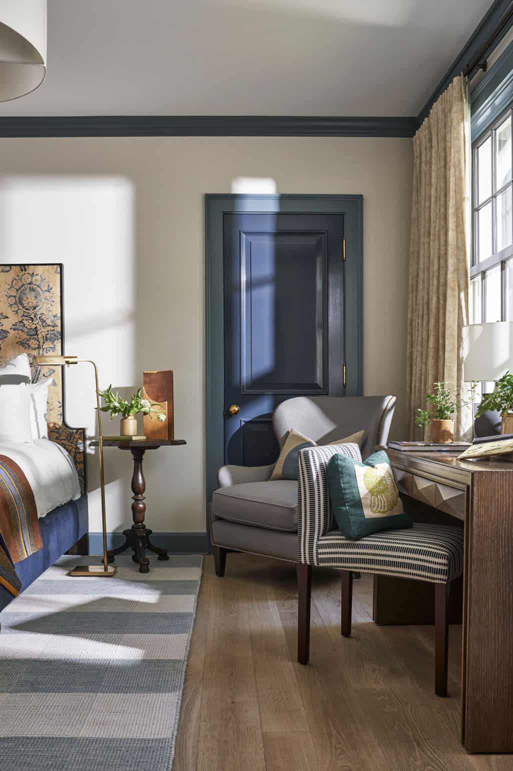Guest bedroom with warm neutral walls, dark teal trim, navy door, and layered textiles