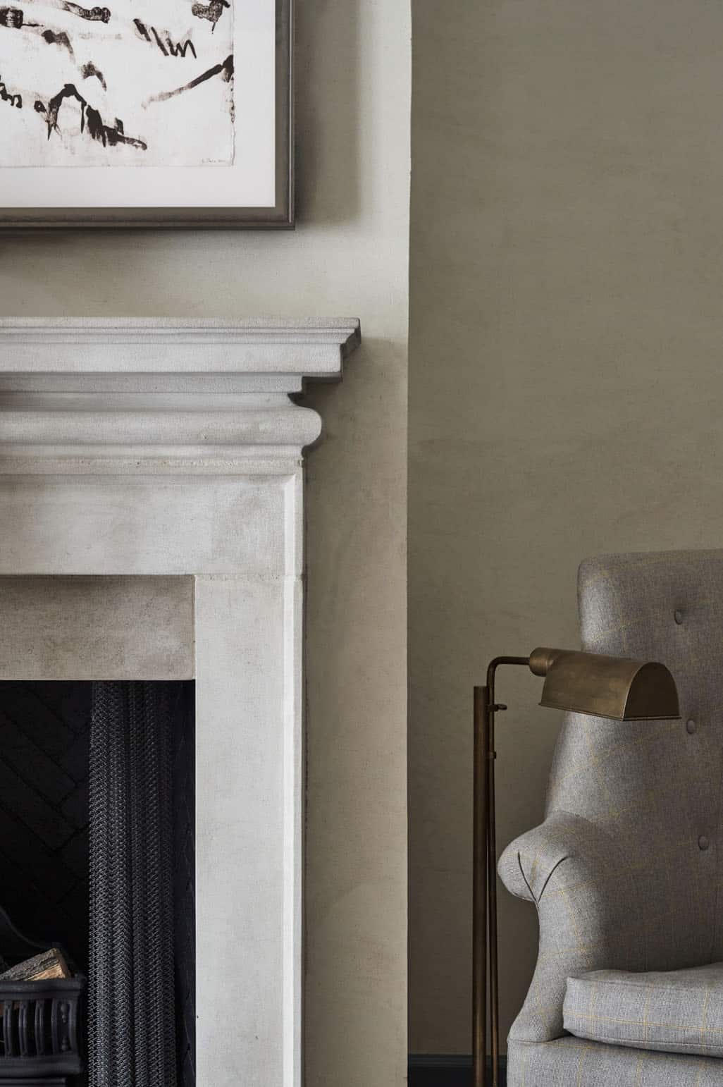 Stone fireplace surround with brass floor lamp and upholstered armchair against olive plaster wall