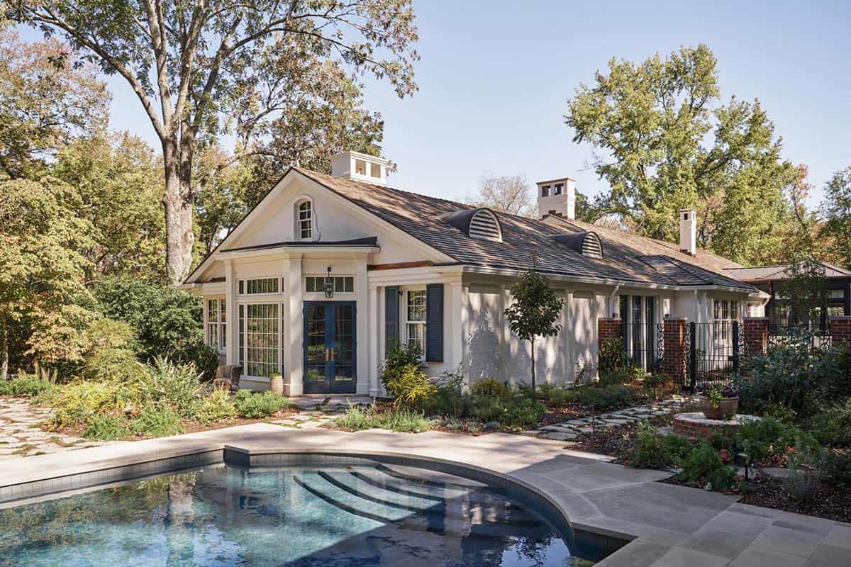 Pool house with colonial architecture, arched dormers, blue French doors, and curved pool in foreground