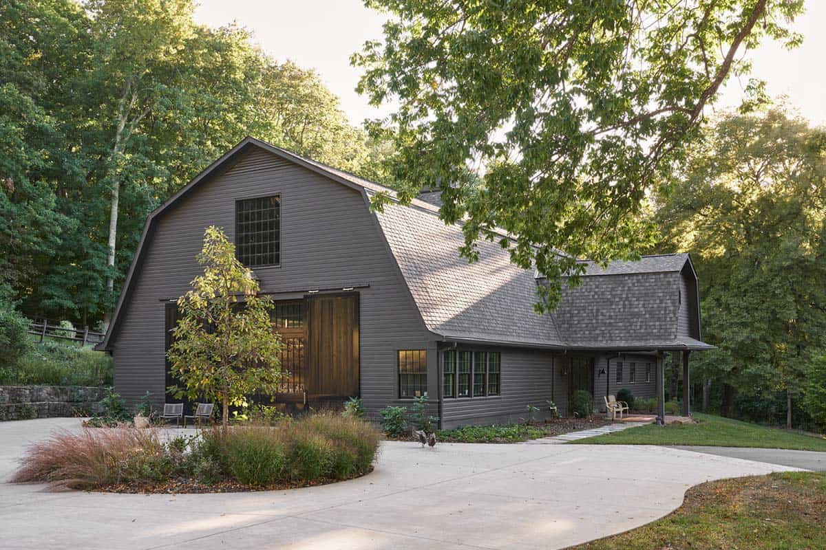 Dark gray gambrel-roof barn conversion with sliding wood doors and ornamental grass landscaping