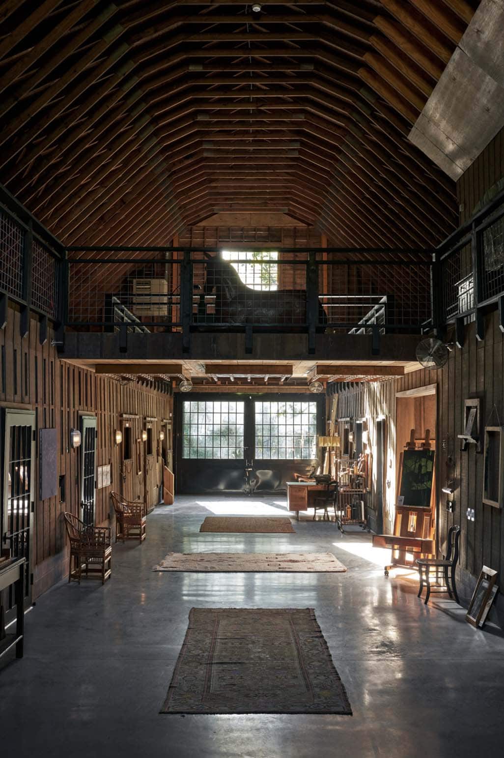 Converted barn interior with soaring wood truss ceiling, concrete floors, mezzanine loft, and artist studio space