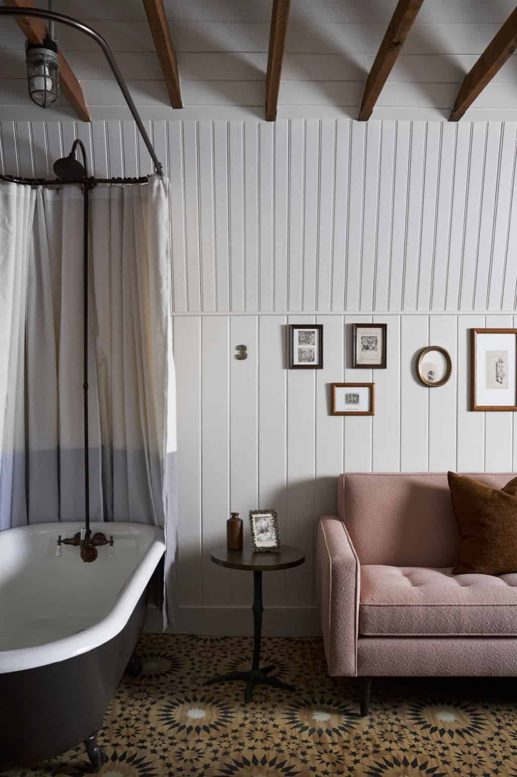 Barn loft bathroom with clawfoot tub, exposed beams, beadboard walls, gallery of small framed prints, and pink sofa
