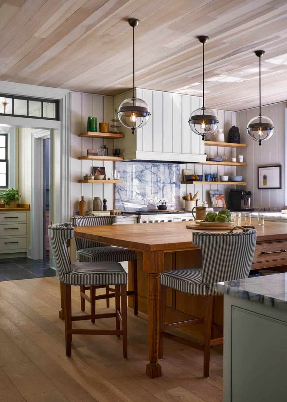 Kitchen with wood island, striped counter stools, globe pendant lights, open shelving, and marble range backsplash