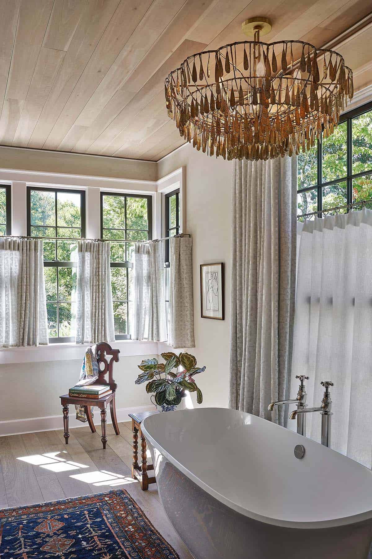 Primary bathroom with freestanding soaking tub, sculptural bronze chandelier, linen curtains, and wood plank ceiling