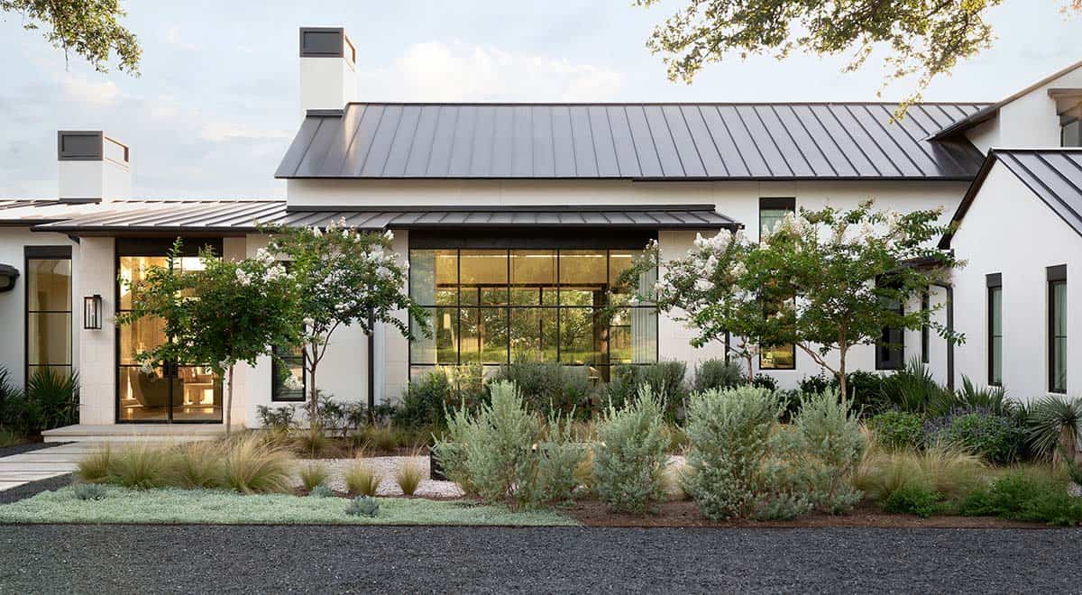 Modern Texas farmhouse exterior with white stucco, black-framed steel windows, metal roof, and native drought-tolerant landscaping