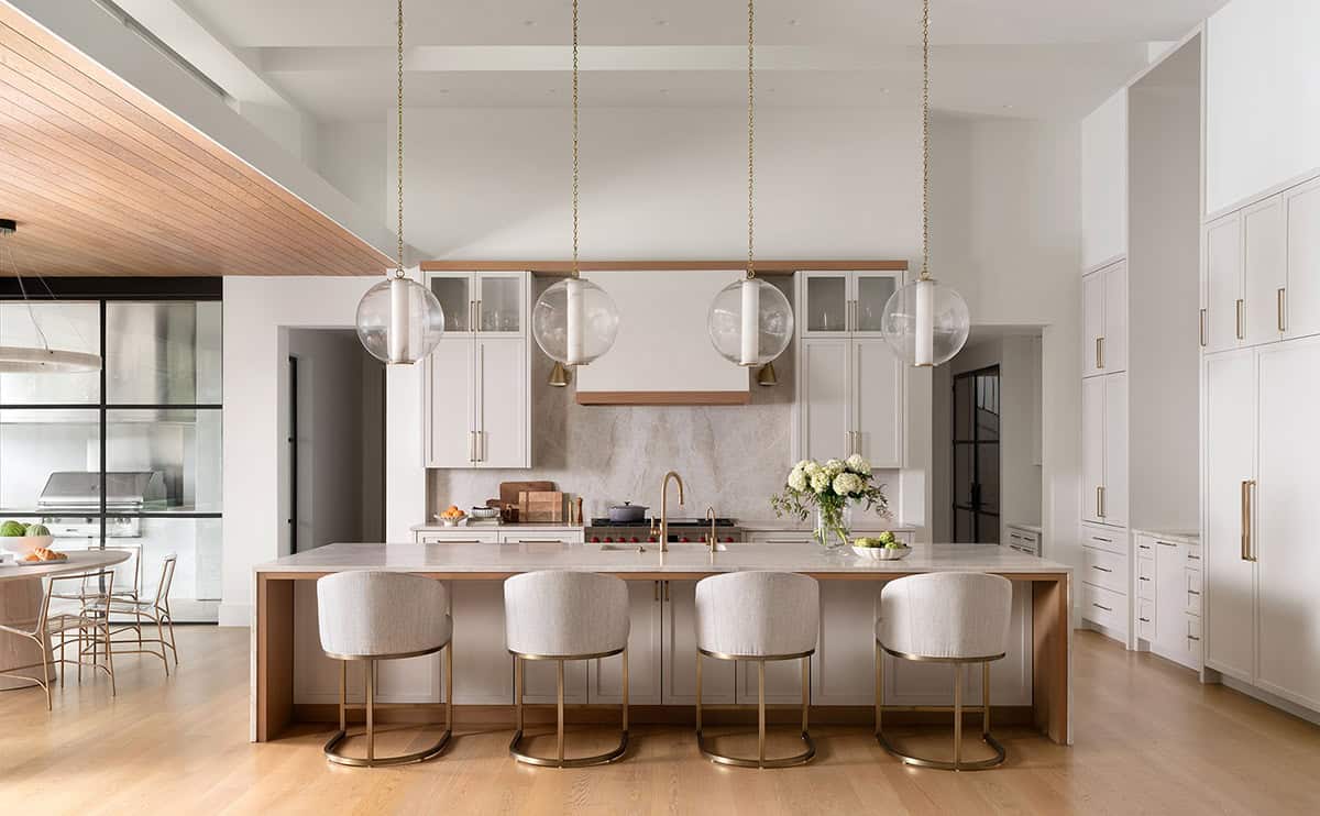 Luxury kitchen with large wood-trimmed island, brass barstools, globe pendant lights, and marble backsplash