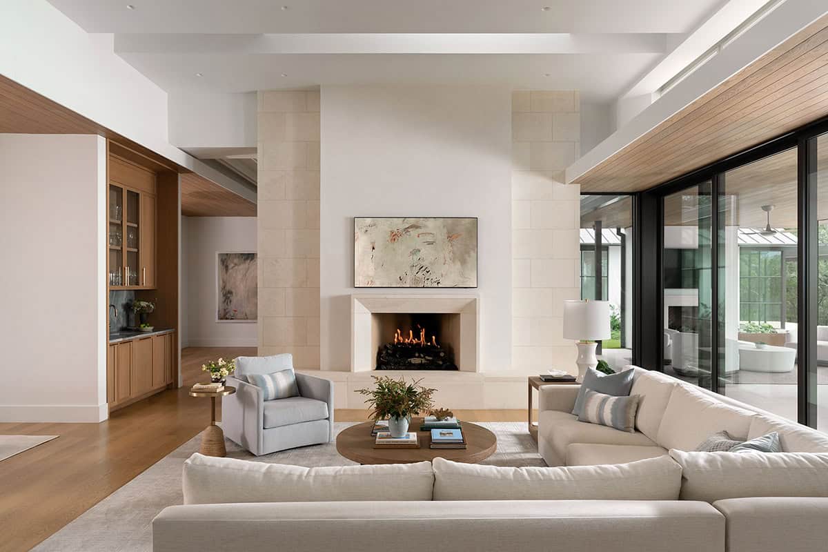 Open-plan living room with limestone fireplace surround, cream sectional sofa, and sliding glass doors to patio