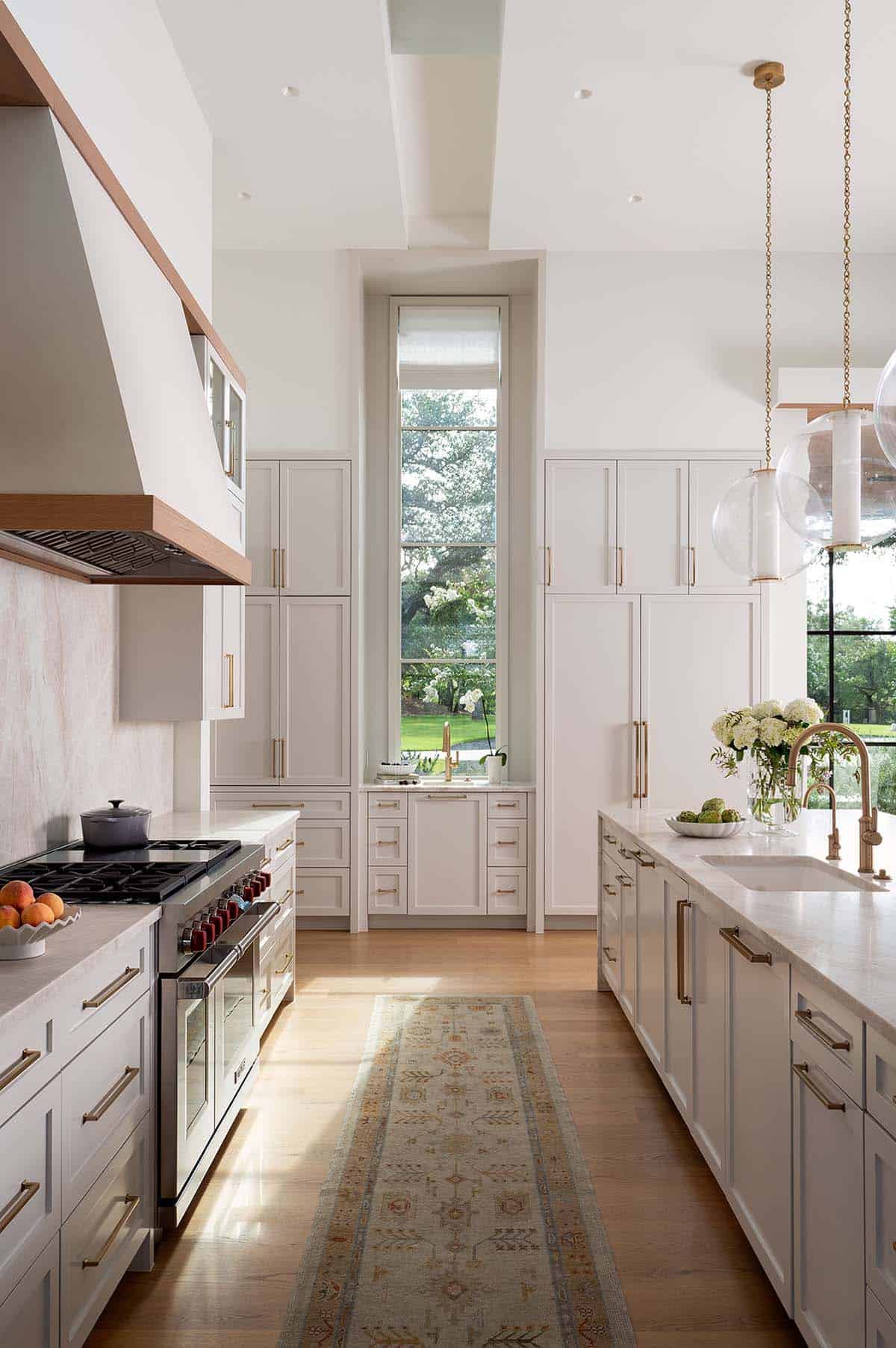 White kitchen with floor-to-ceiling cabinetry, brass hardware, professional range, and tall arched window