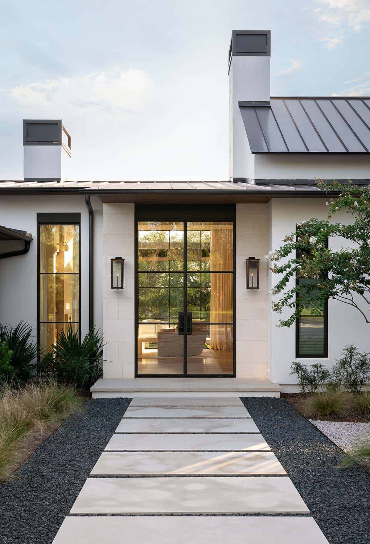 Steel-framed glass front entry doors with stone pathway, flanking lantern sconces, and gravel garden