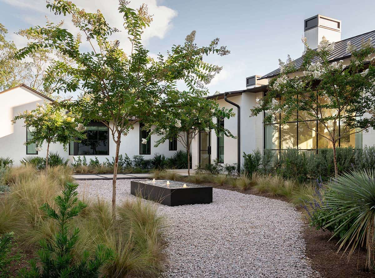 Courtyard garden with gravel path, black rectangular water feature, ornamental grasses, and white stucco facade