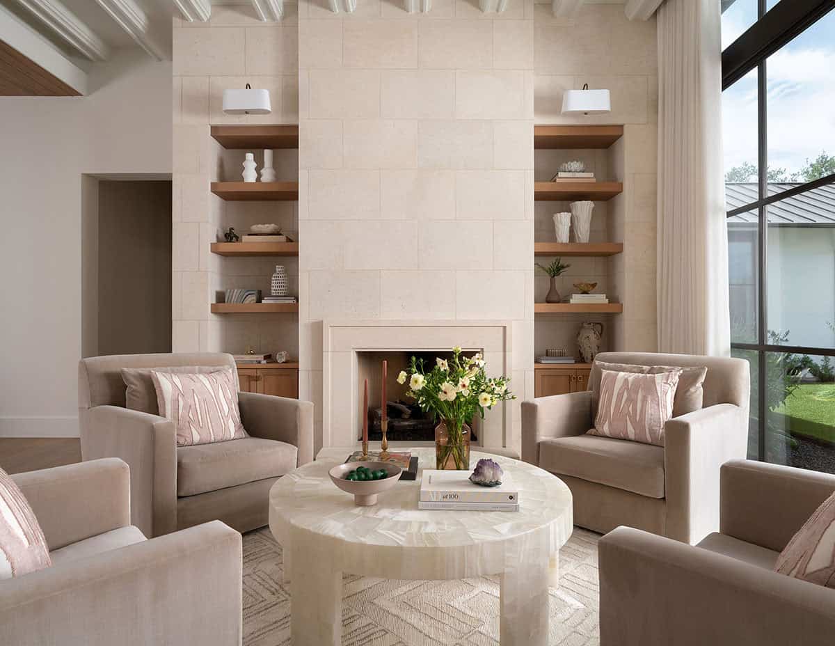 Formal living room with limestone fireplace, flanking oak bookshelves, taupe club chairs, and steel-framed windows