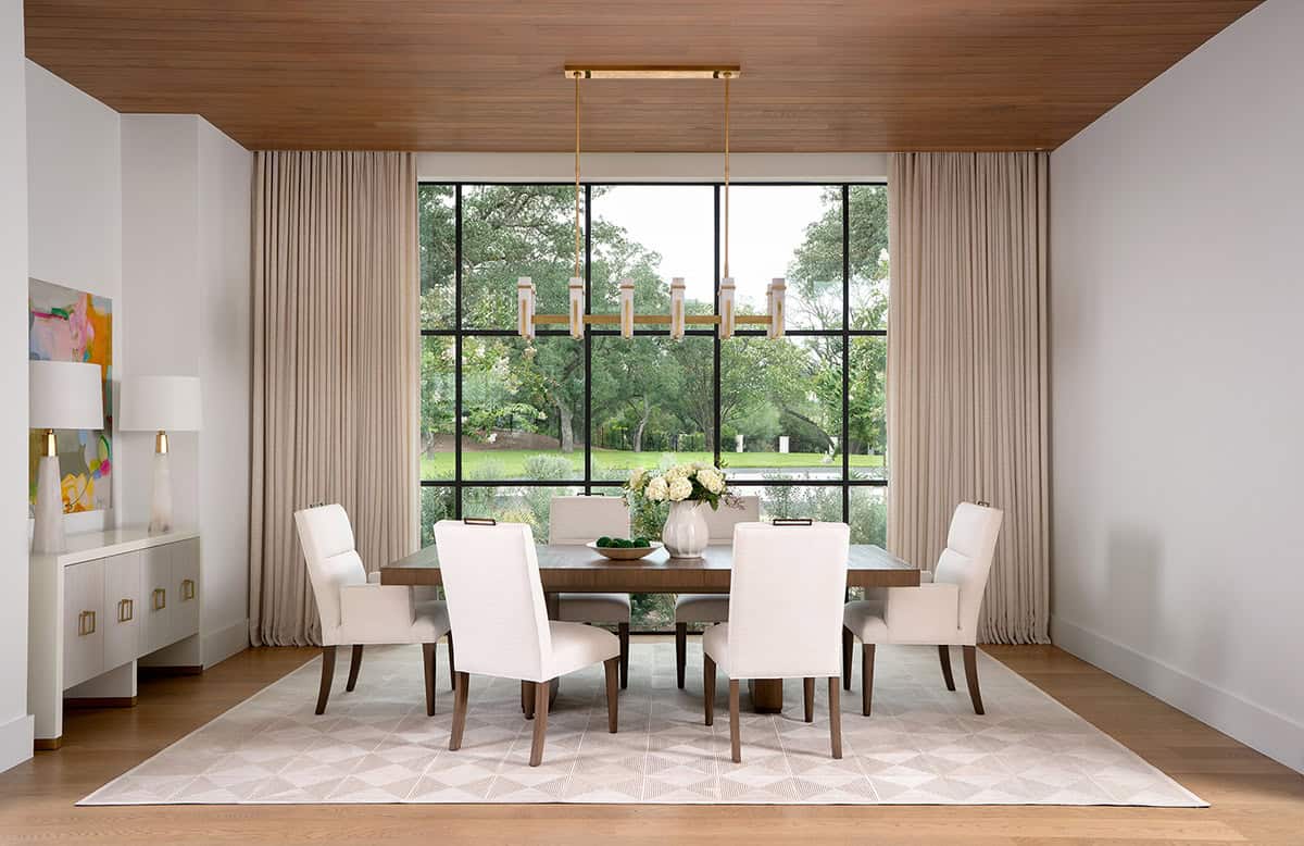 Formal dining room with wood-paneled ceiling, steel-framed picture window, walnut table, and brass chandelier