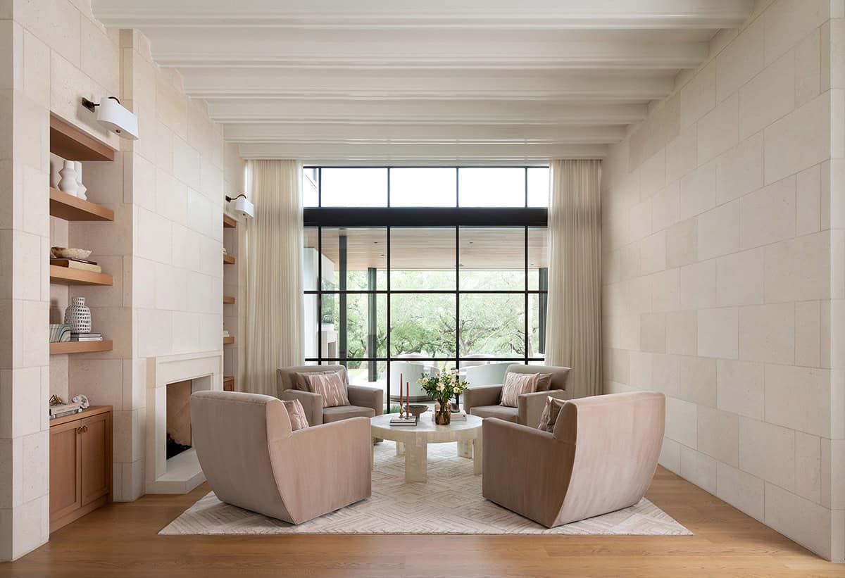Intimate sitting room with floor-to-ceiling limestone tile walls, fireplace, taupe armchairs, and steel-framed window
