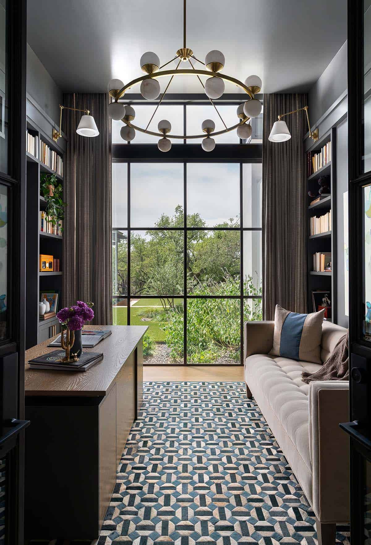 Home office library with dark built-in bookshelves, steel-framed window wall, geometric rug, and brass Sputnik chandelier
