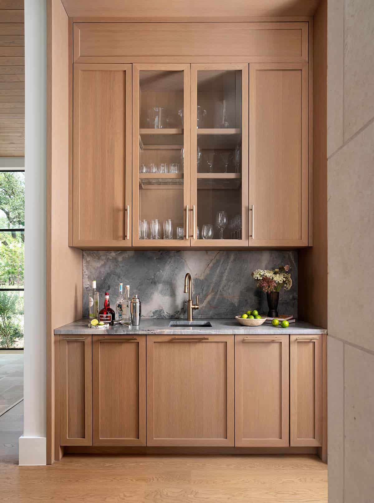 Built-in wet bar with natural oak cabinetry, dramatic quartzite slab backsplash, and brushed brass faucet