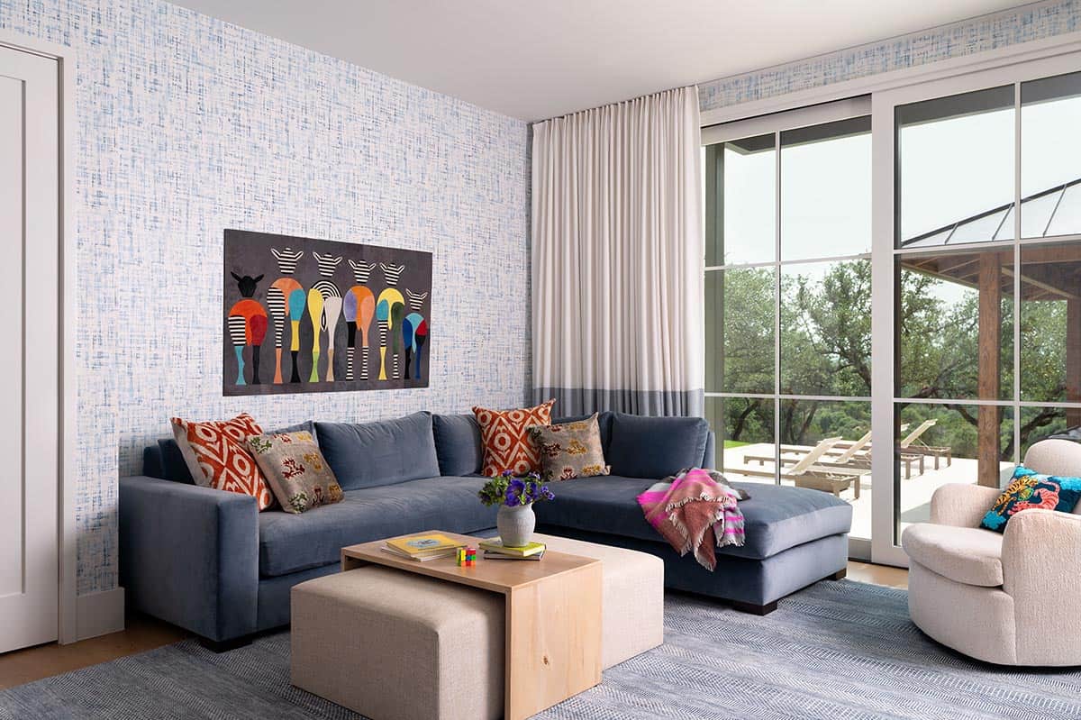 Playful family room with navy sectional sofa, blue textured wallpaper, colorful abstract artwork, and glass doors to outdoor patio