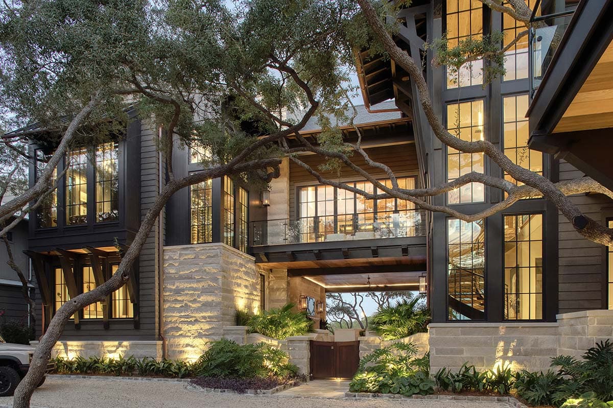 Lake house facade with steel frame windows stone base and mature oak trees