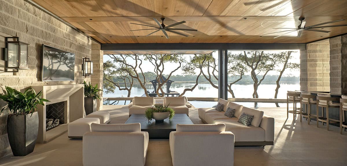 Open air living room with wood ceiling stone walls lake views and large ceiling fans