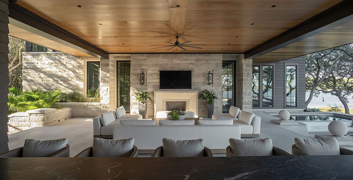 Covered outdoor living room with stone fireplace wood ceiling and pool views