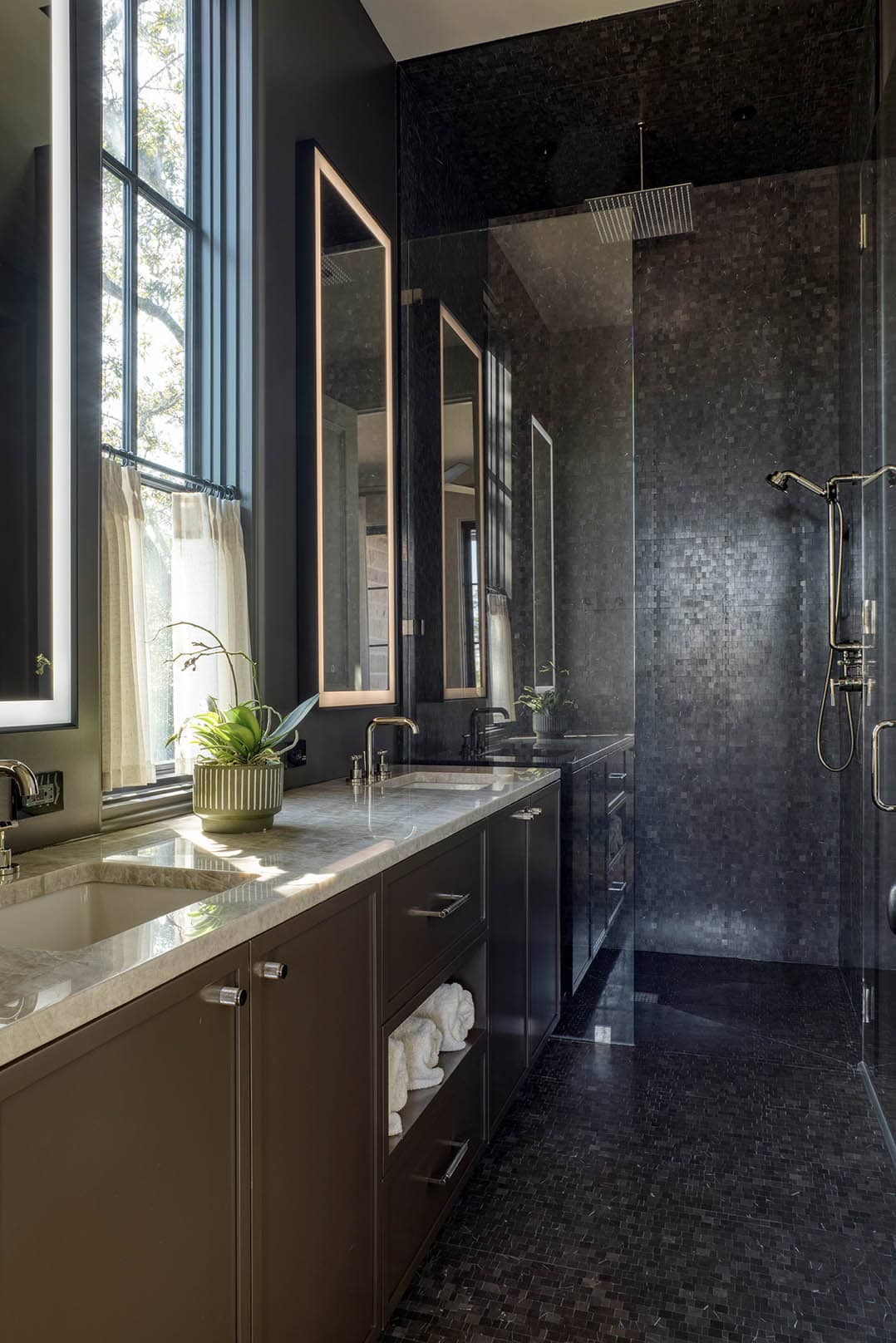 Dark bathroom with black mosaic tile double vanity and glass shower