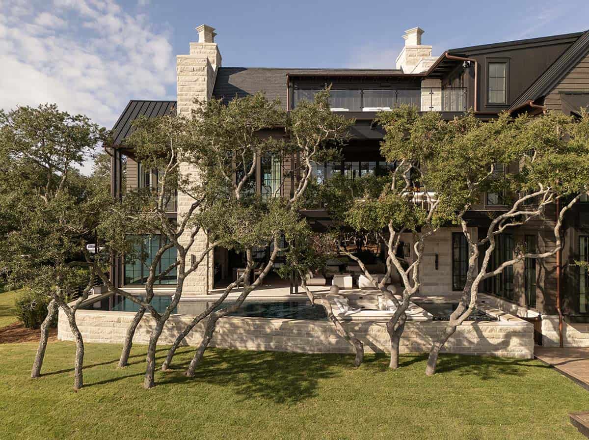 Lake house rear exterior with pool oak trees and stone chimney towers