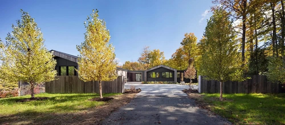 Aerial front view of modern Vermont ski house with dark siding and gravel driveway surrounded by autumn trees